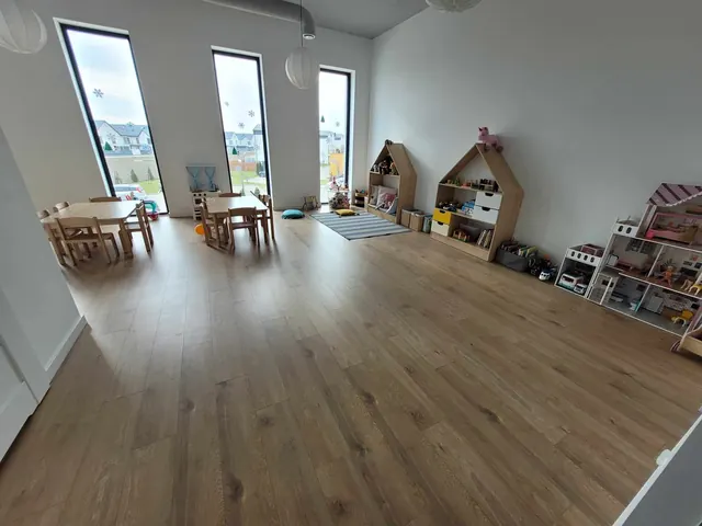 Przestronna sala przedszkolna z drewnianymi domkami i stolikami